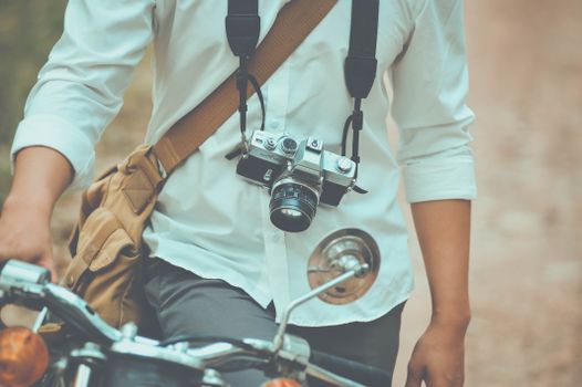 Person wearing a vintage camera around the neck and holding motorcycle handlebars, ready for adventure.