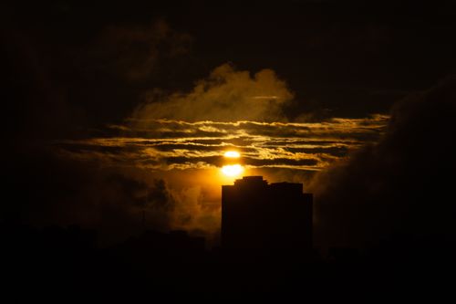 Free A striking image of city buildings silhouetted against a vibrant sunset with dramatic clouds. Stock Photo