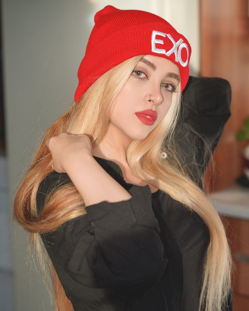 Free A fashionable woman with red lips poses indoors wearing a red beanie and black attire. Stock Photo