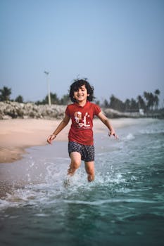 Young girl in red shirt enjoying a playful run along the shore at a sunny beach.