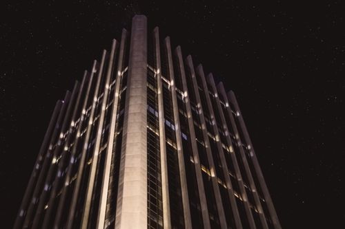Free From below exterior of contemporary multistory house with glowing lights located on street in city against dark sky at night time Stock Photo