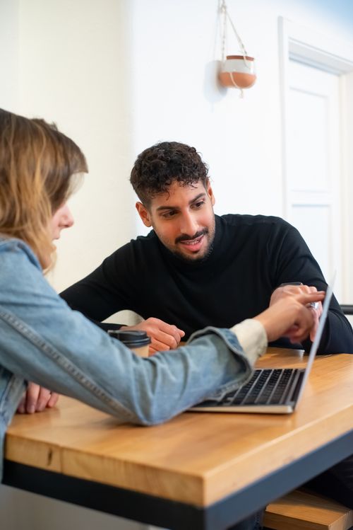 Free Young professionals engage in a collaborative discussion around a laptop in a modern office setting. Stock Photo