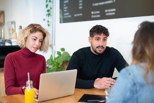 Diverse group collaborating in a modern office setting with laptops and drinks.