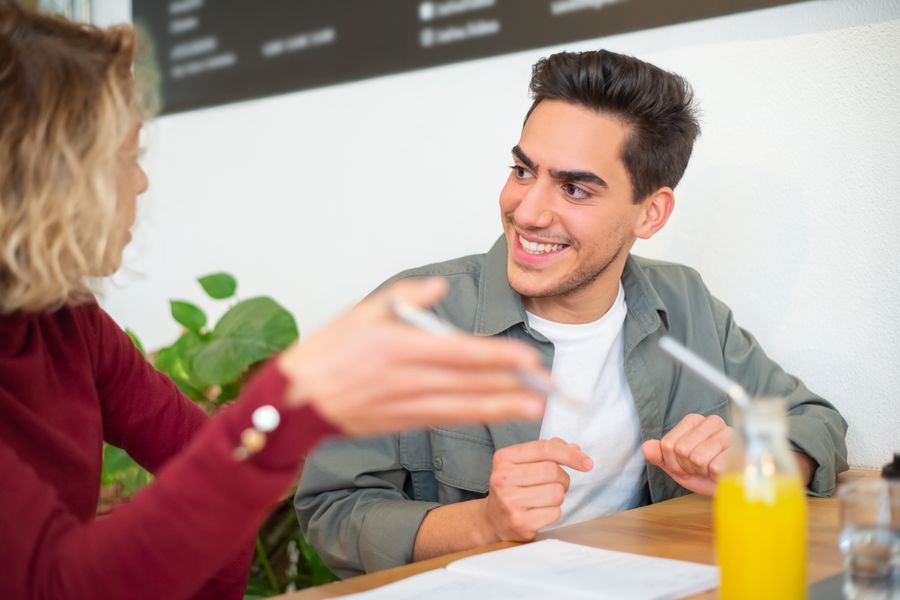 Two young adults having a positive discussion inside a cozy café setting, enjoying drinks.