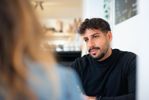 Free Portrait of a thoughtful man with a beard in a cafe setting, wearing a black shirt. Stock Photo
