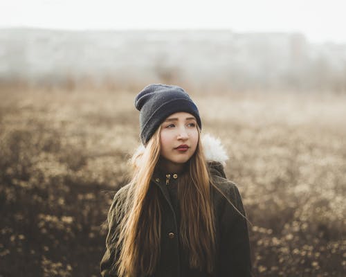 Serious stylish female in cap looking away thoughtfully while spending time in nature