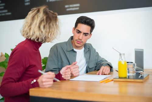 Free Two young adults engaged in conversation at a café, focused on a document. Stock Photo
