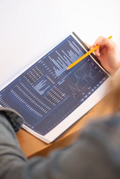 A close-up of a person analyzing blue graph data with a yellow pencil.