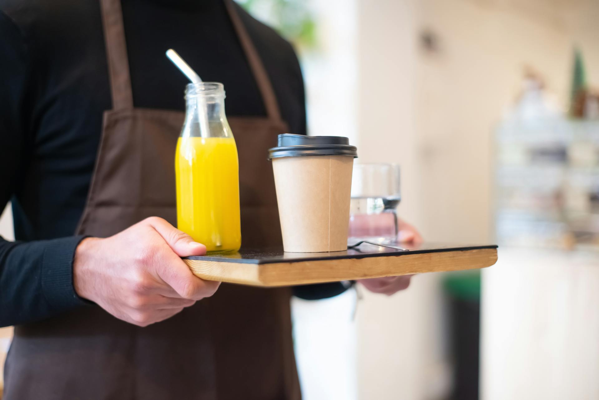 A barista serves juice and coffee on a wooden tray in a cozy café setting.