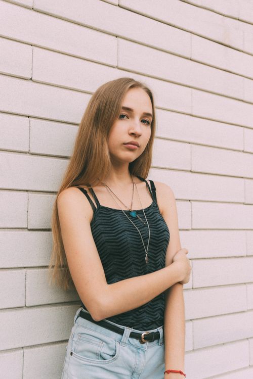 Free Young female with long hair looking at camera in casual trendy summer outfit near modern wall Stock Photo