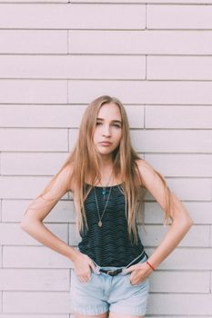 Trendy young female with fair long hair looking at camera near white contemporary wall