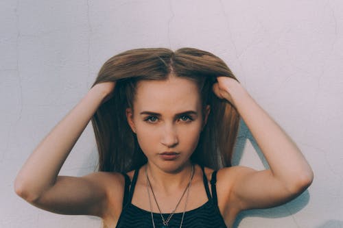 Young slender woman touching hair near white wall