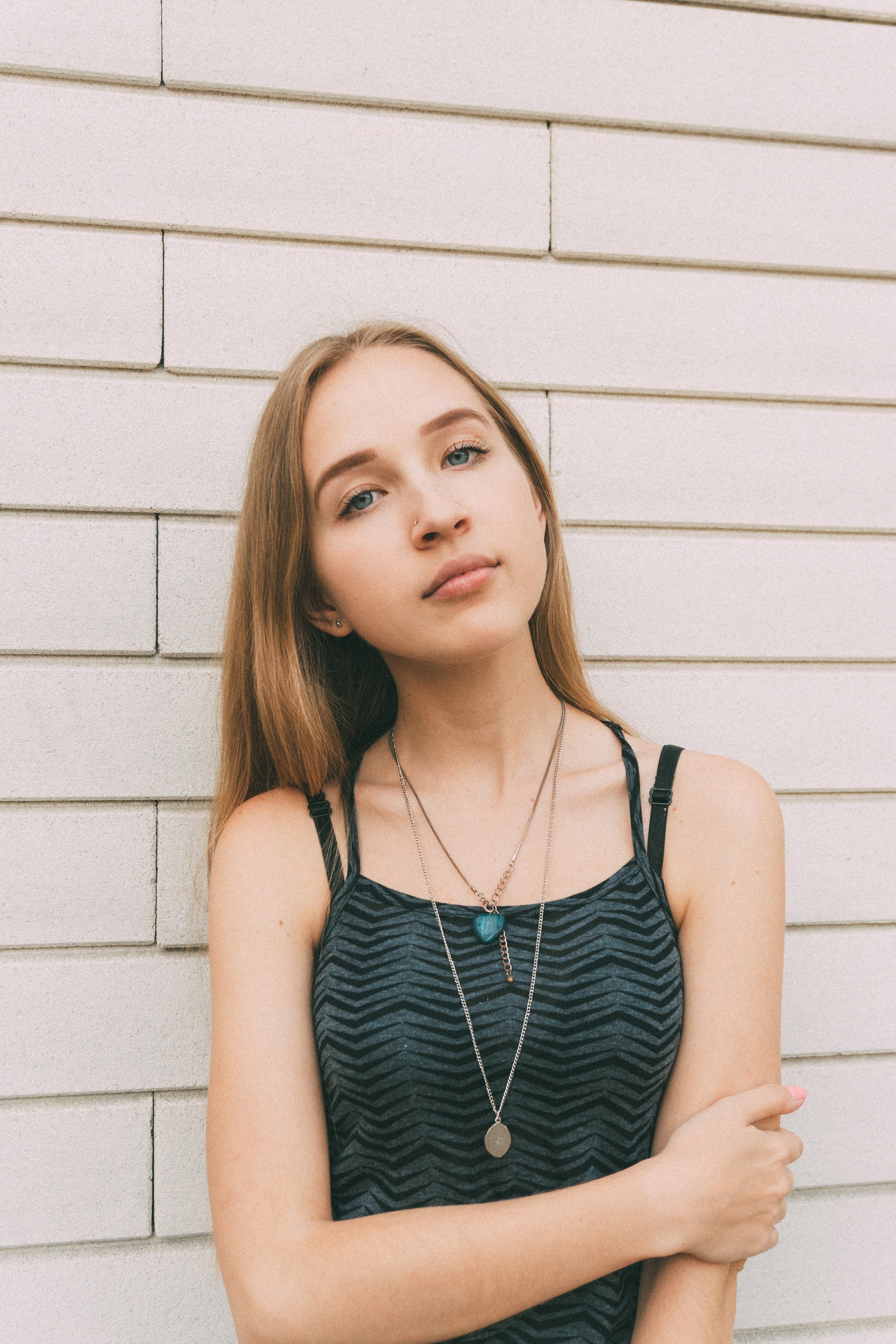 Young confident slender female touching arm and looking at camera near modern brick white wall