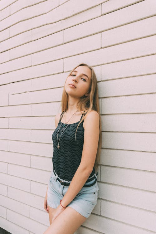 Young female with fair long hair looking at camera while leaning on wall of urban building