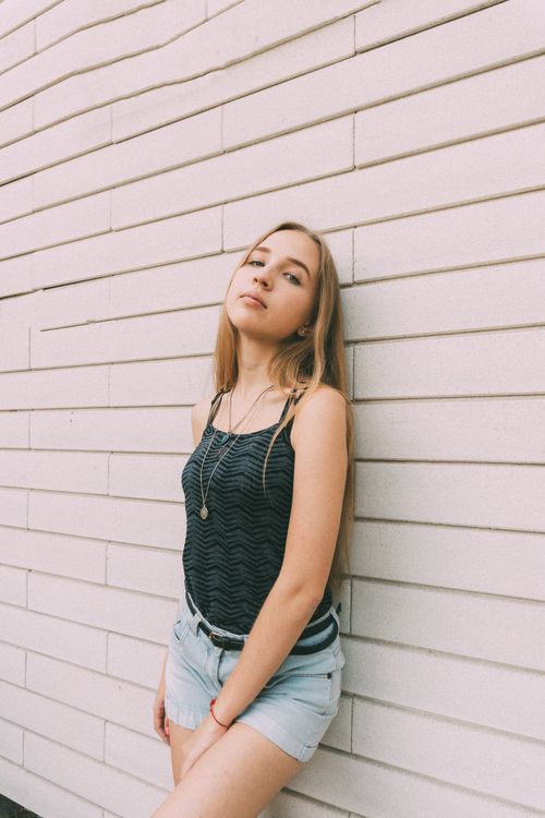 Free Young female with fair long hair looking at camera while leaning on wall of urban building Stock Photo