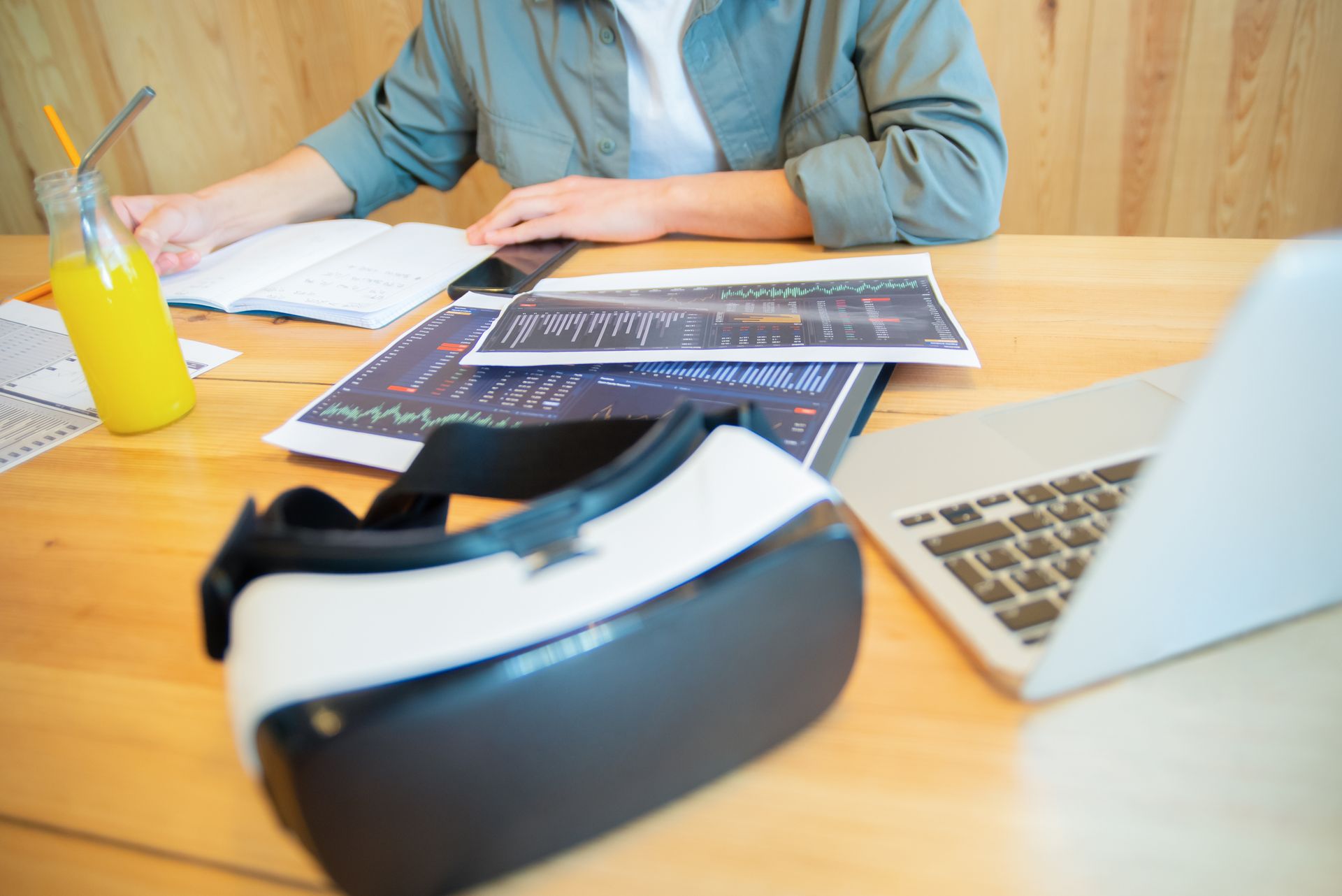 A workspace featuring VR goggles, laptop, analytics papers, and juice, illustrating modern business tools.