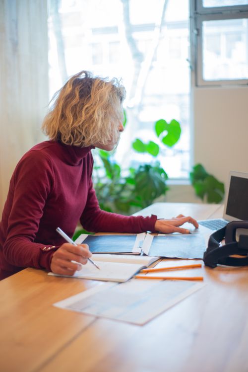 Free Focused woman in a turtleneck sweater working at a desk in a bright office with natural light. Stock Photo