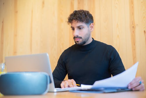 Free A Man Working with Documents Using a Laptop Stock Photo