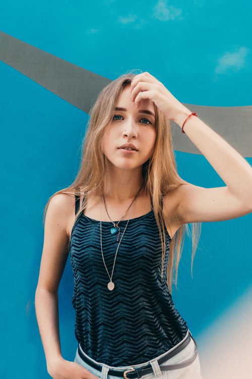 Free Young female with long hair in trendy clothes looking at camera near blue wall with stripe Stock Photo