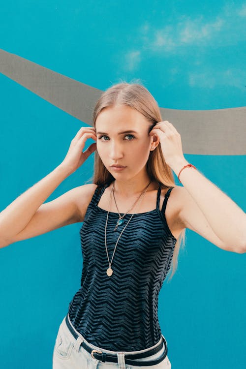 Young female touching long fair hair while looking at camera near blue wall with gray curve