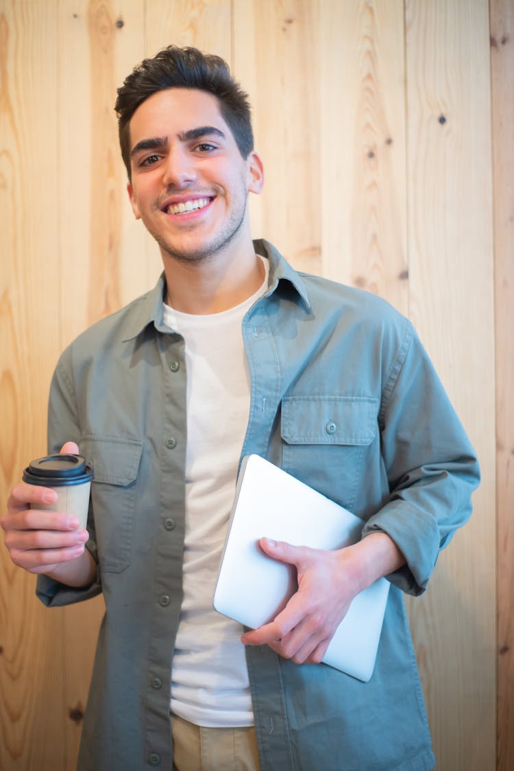 A Smiling Man Holding A Coffee Cup And A Laptop