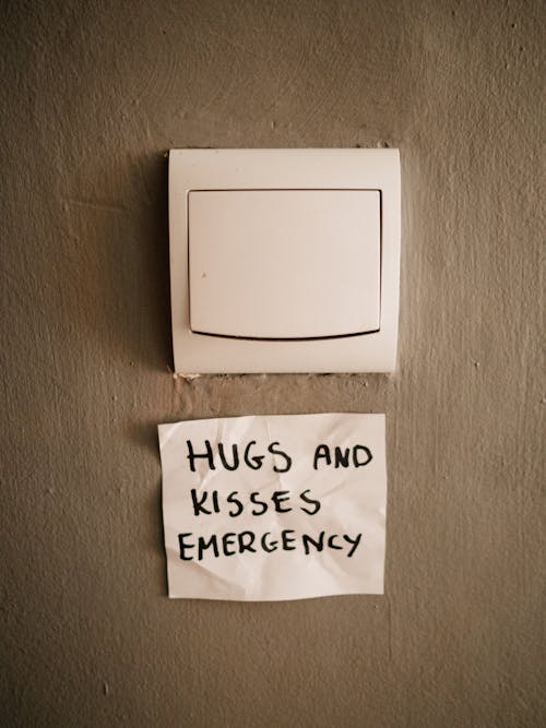 Lighting switch on wall near attached paper with Hugs and Kisses Emergency inscription