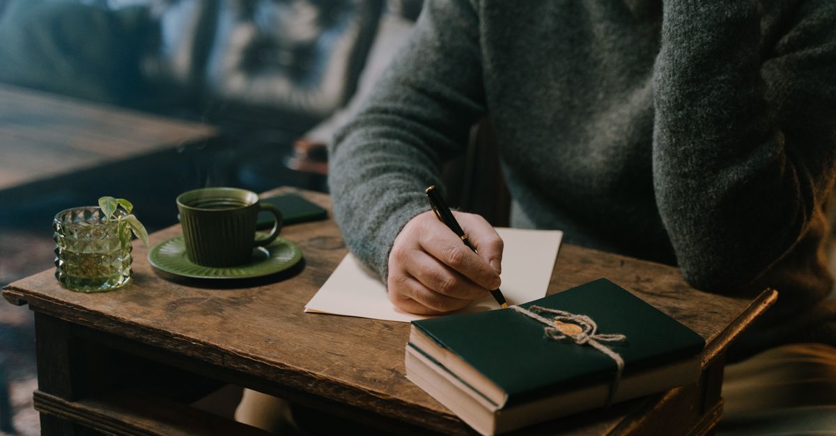 A person sitting at a cafe table with a smartphone and a paper map, looking thoughtfully at a handwritten list of places, natural lighting