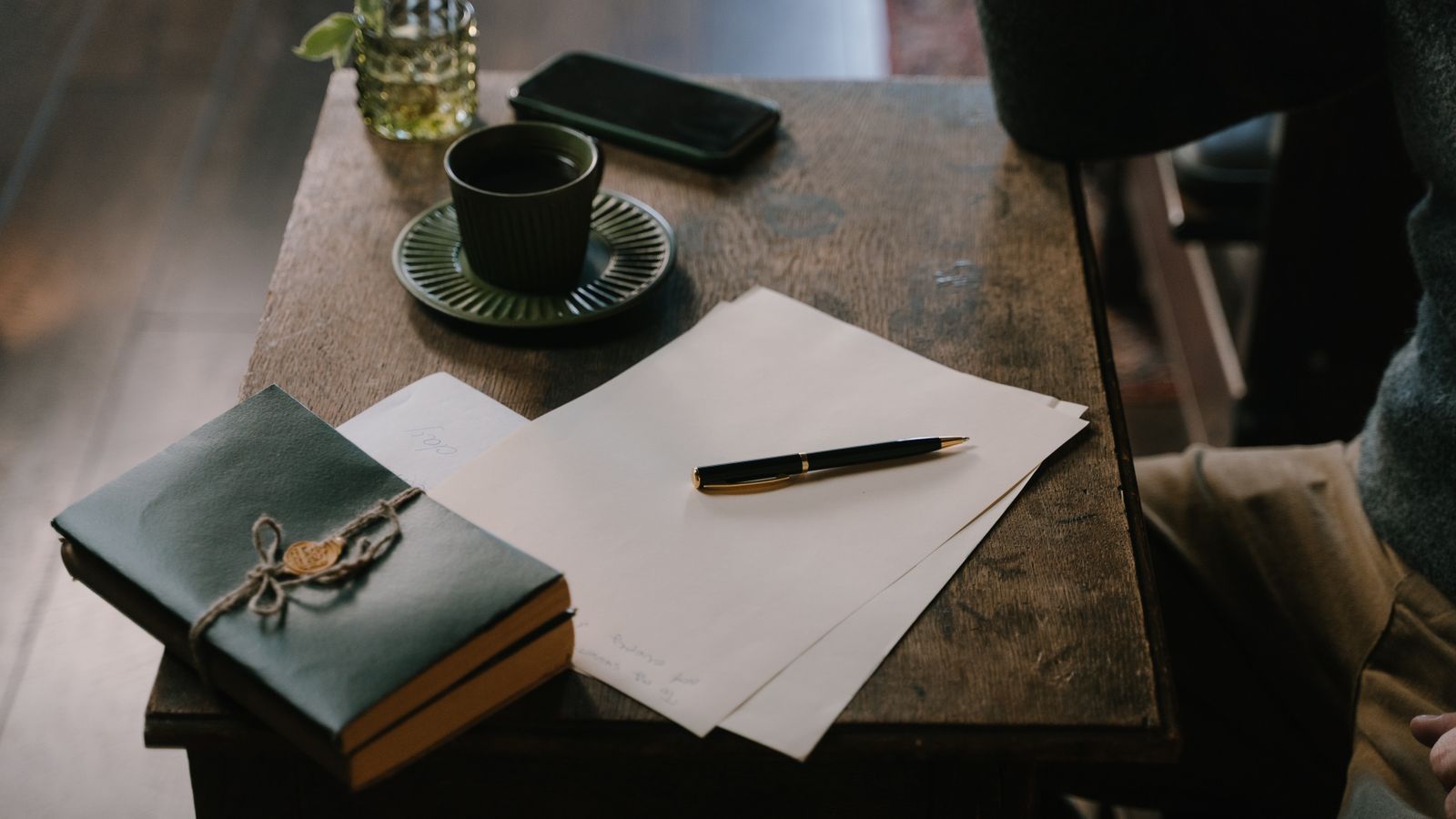 Pen on paper beside books and a coffee cup on a wooden table