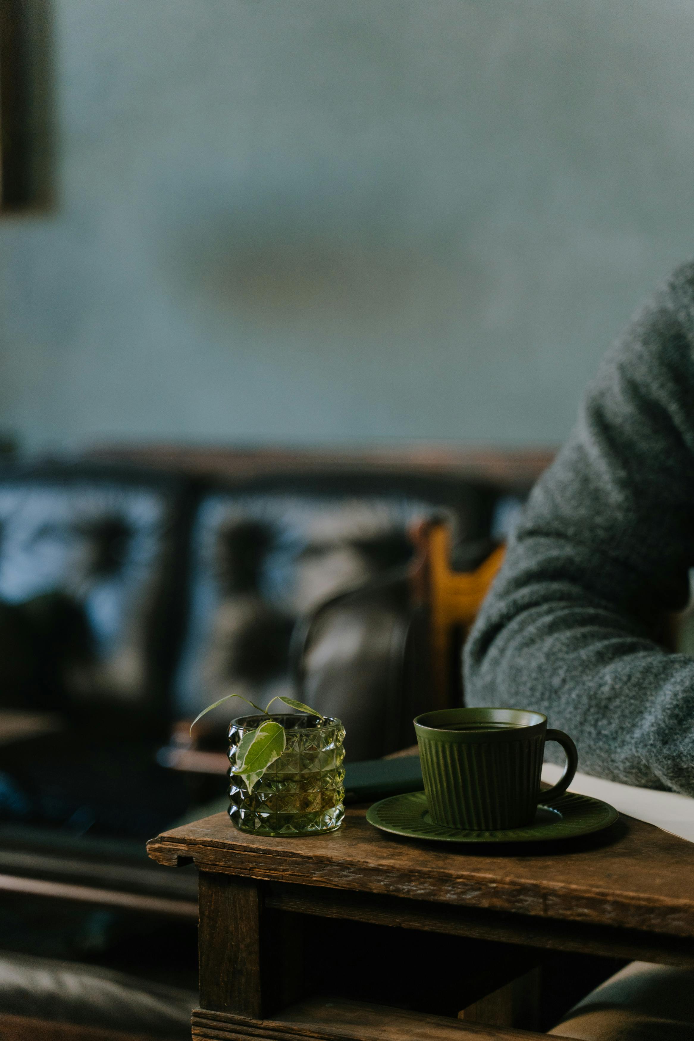 A wooden table with a green cup and iced drink in a cozy lounge setting.