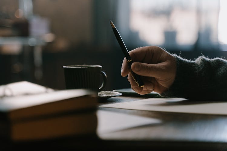 A Hand Holding A Pen Near Cup And Saucer