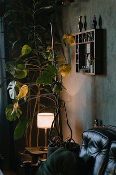 Warm living room interior featuring a leather sofa, lush plants, and modern lighting, creating a cozy ambiance.