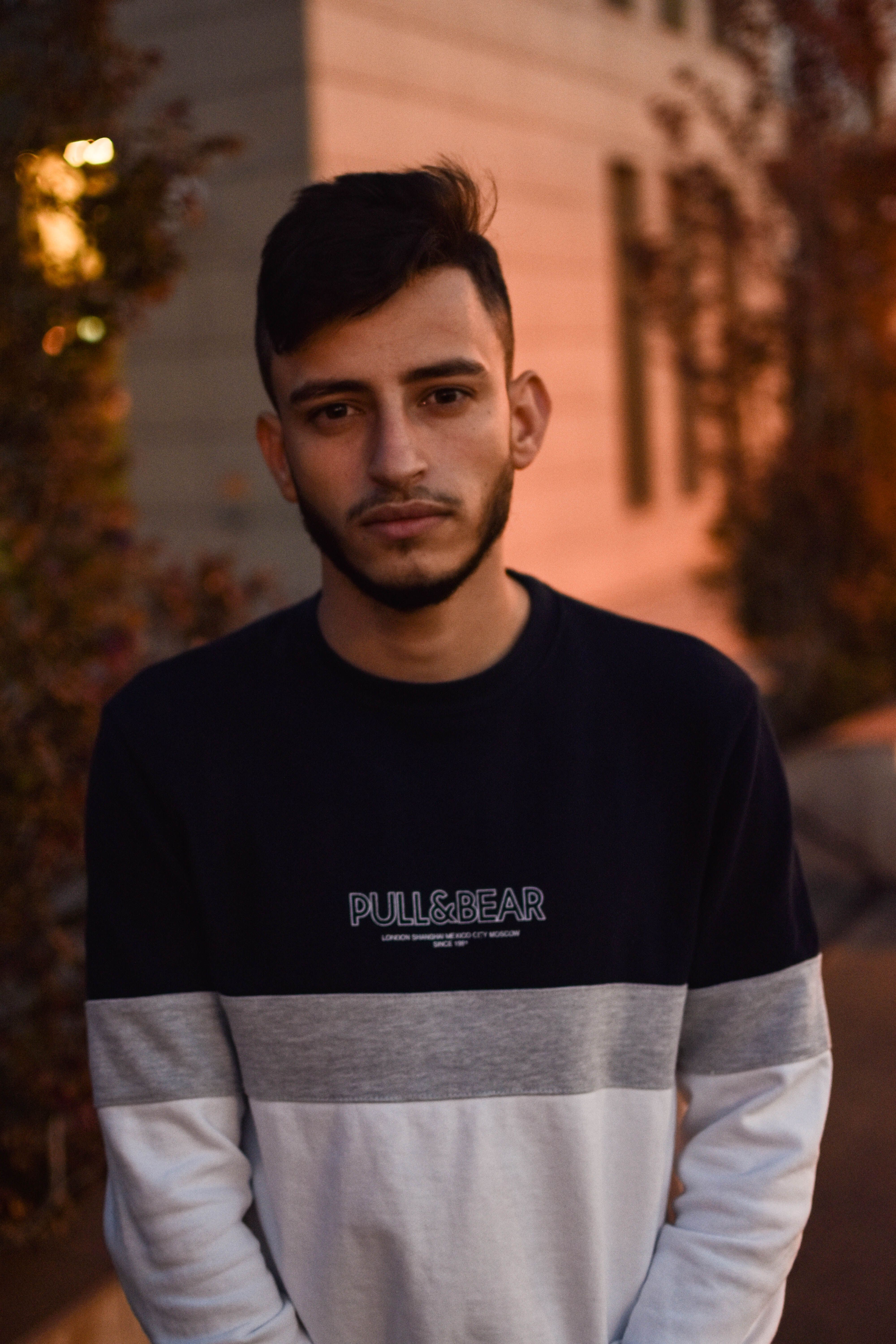 A young man poses in casual wear during golden hour outdoors, showcasing urban fashion.