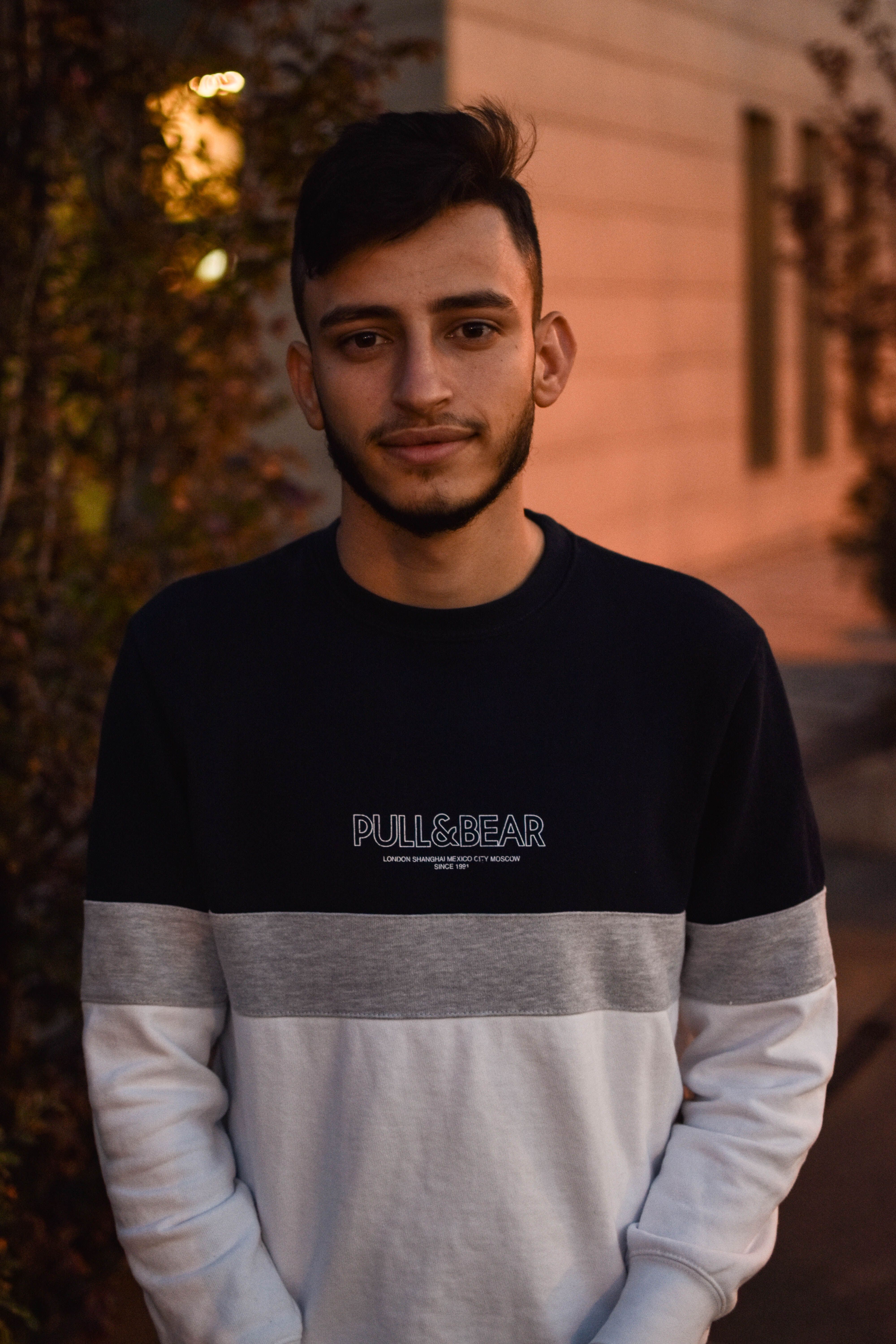 Portrait of a stylish young man with a beard, set in an urban environment during the evening.