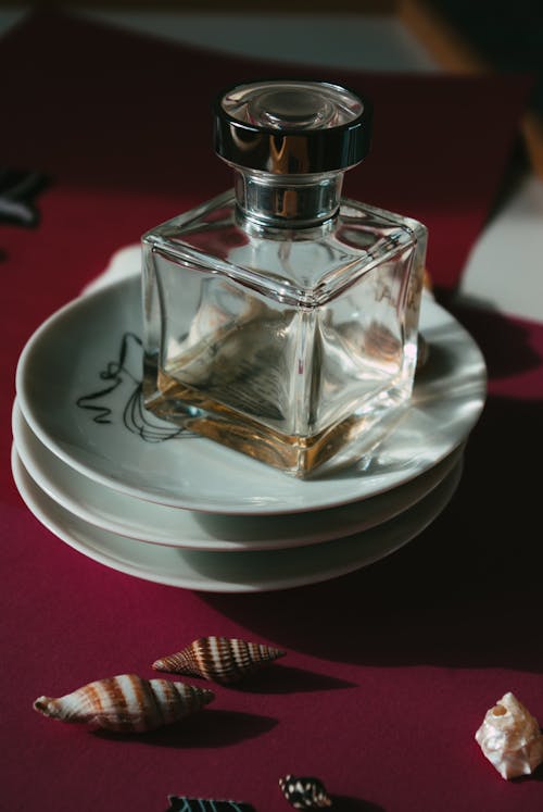 From above of glass bottle of perfume placed on stack of ceramic plates on table decorated with various seashells