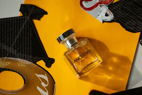 Top view of bottle of perfume placed on yellow surface near magazine clippings in daylight