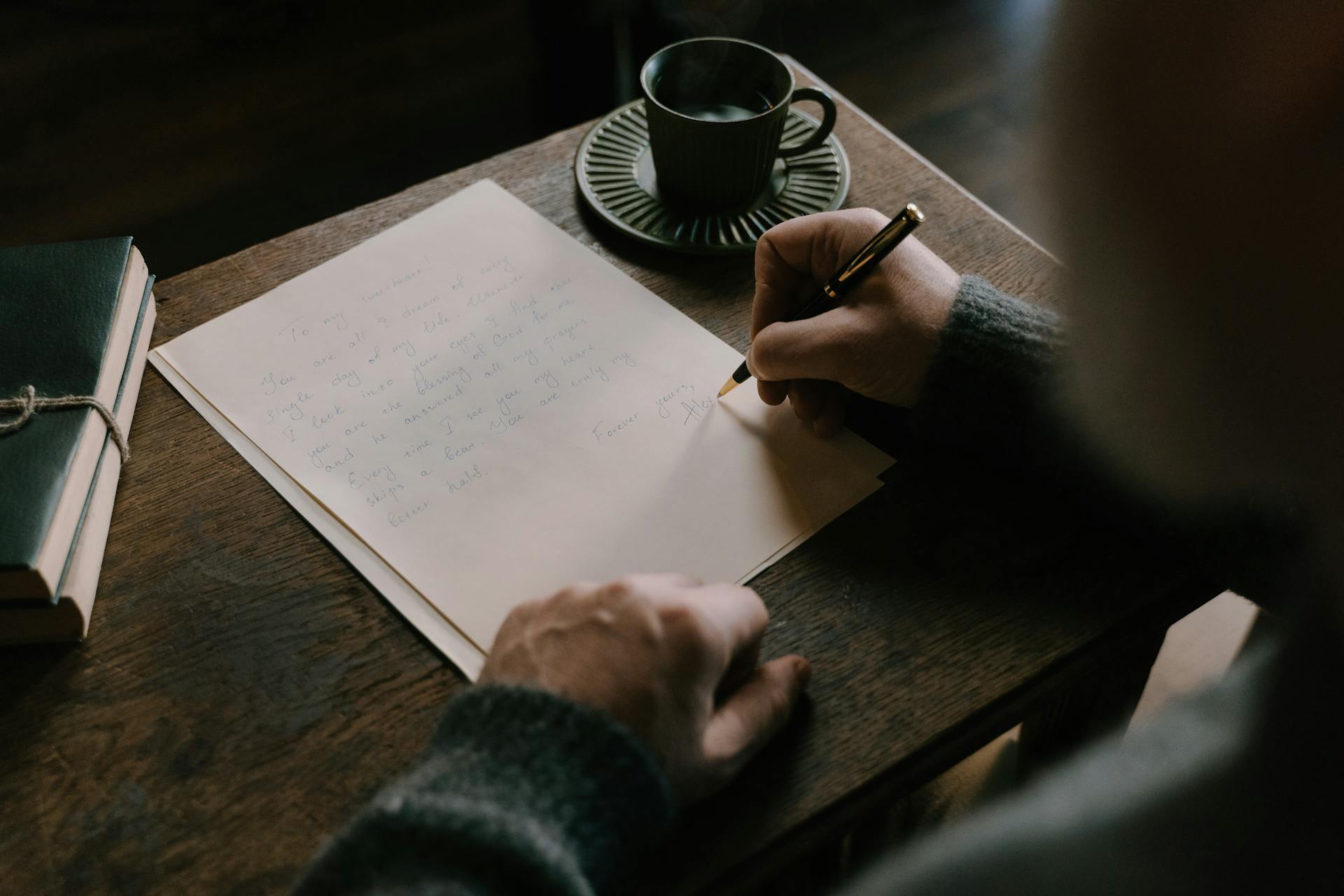 An adult writing a letter on a wooden desk with a cup of coffee, embodying a warm, intimate atmosphere.