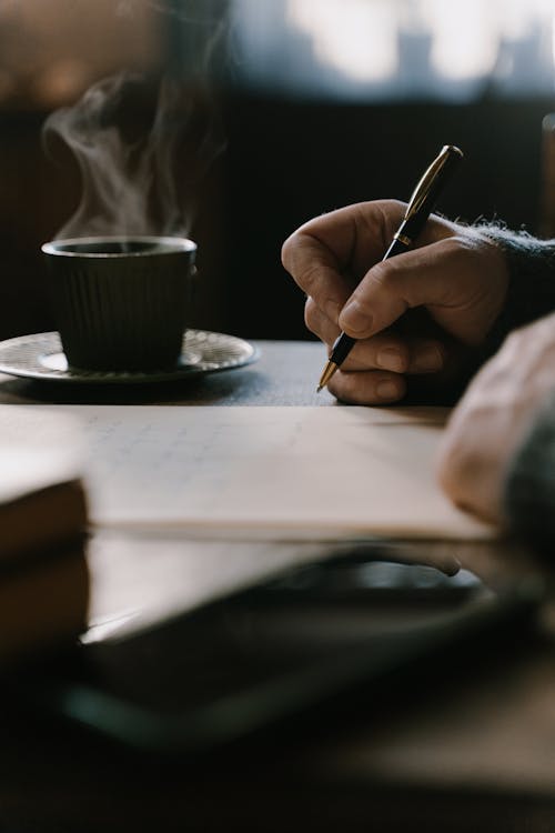 A Person Making a Letter with a Cup of Smoking Coffee Nearby