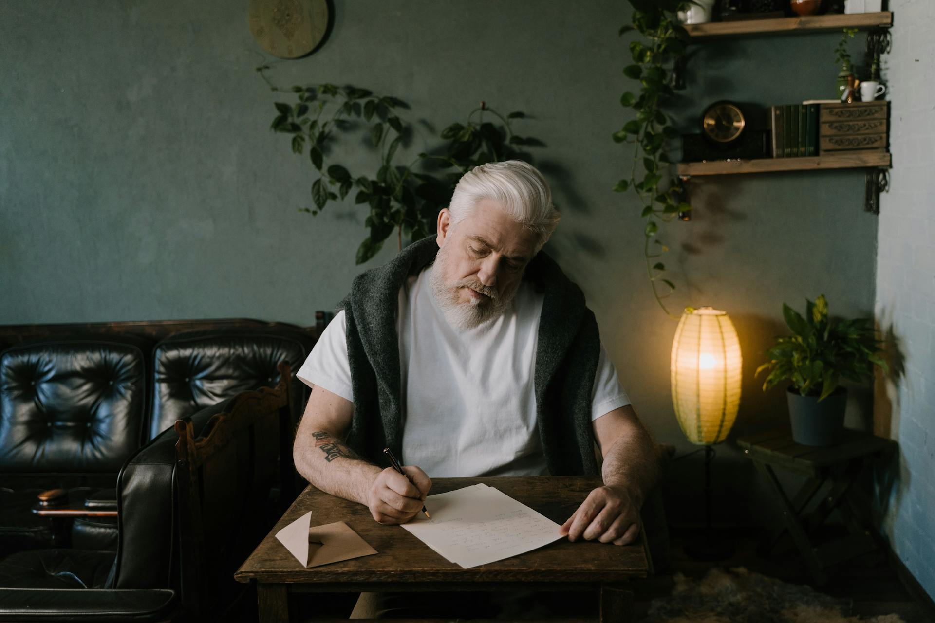 Senior man pens a letter at a wooden table in a cozy home interior.