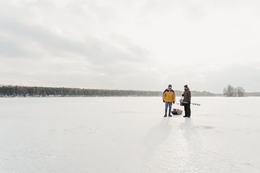 Two people ice fishing on a snow-covered frozen lake in winter.