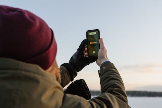 Man holding a smartphone outdoors, capturing a moment in a winter landscape.