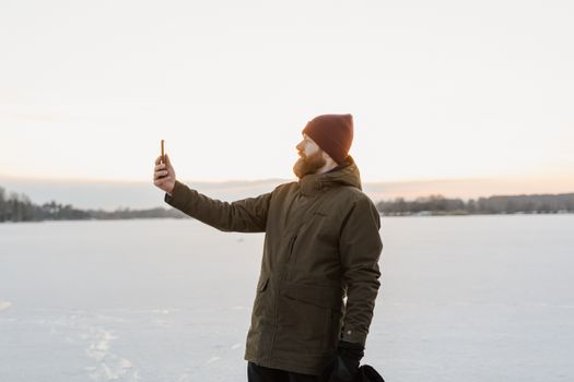A man in winter clothes takes a selfie on a snow-covered, frozen lake during the day.