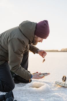 Bearded man ice fishing, holding a fresh catch on snow-covered ground.