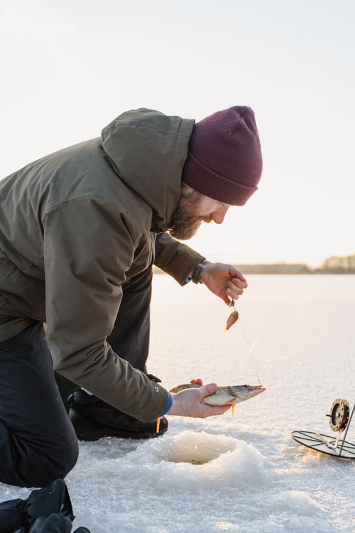 Free Bearded man ice fishing, holding a fresh catch on snow-covered ground. Stock Photo