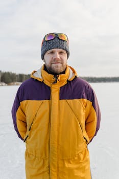 Outdoor portrait of a bearded man wearing winter clothes, standing on a frozen lake with a smile.