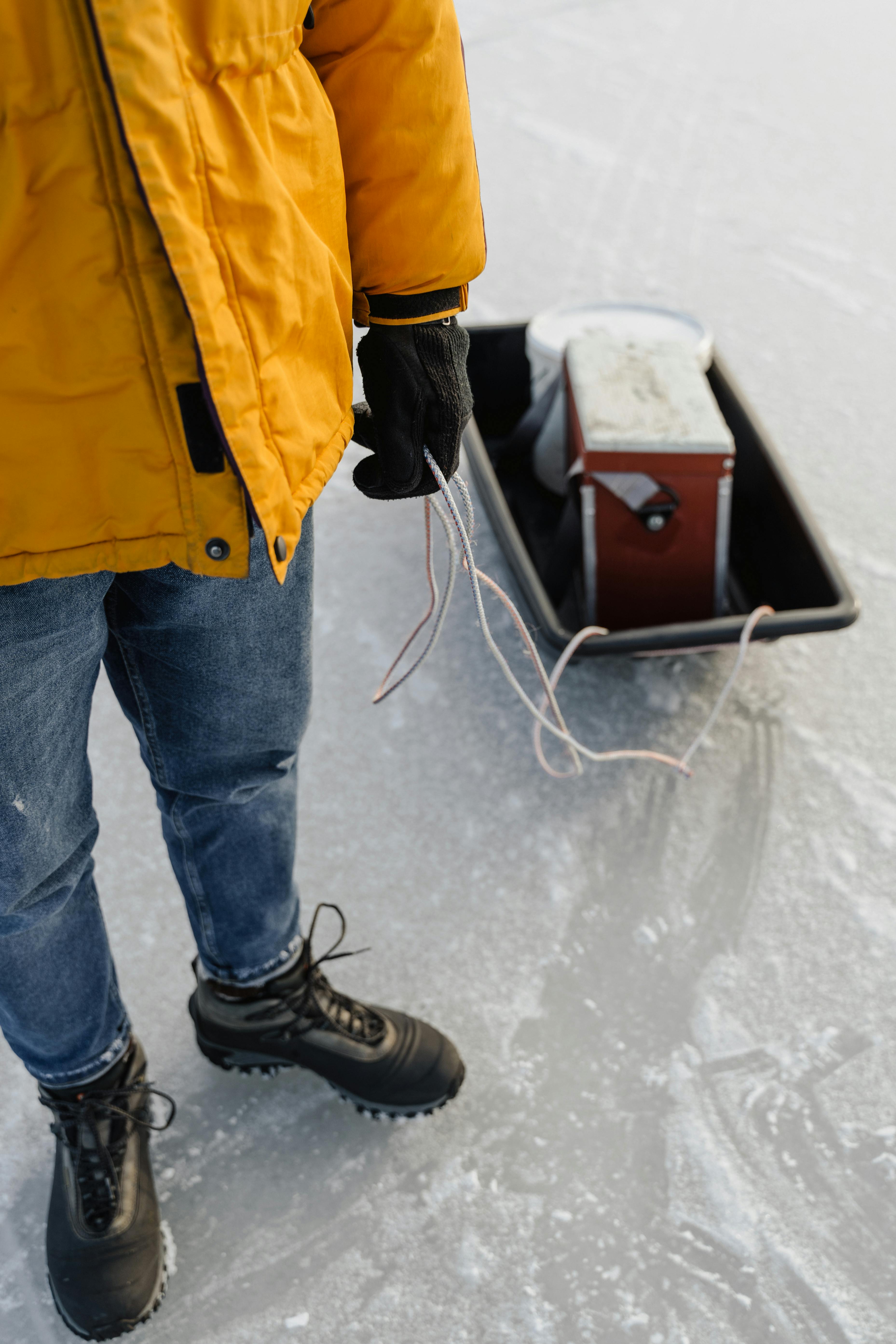 Person in winter gear preparing for ice fishing on a frozen lake with equipment.