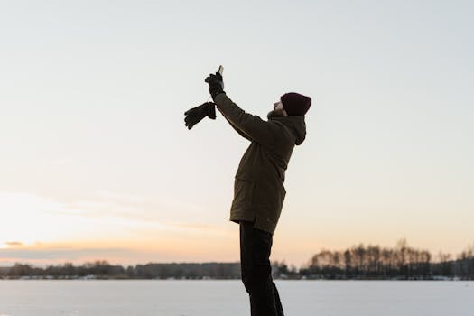 A person in a brown jacket takes a photo outdoors on a snowy winter day.