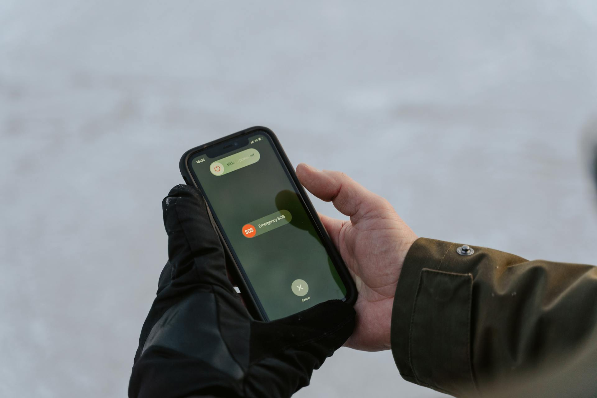 Gloved hands holding a smartphone displaying an emergency SOS screen.