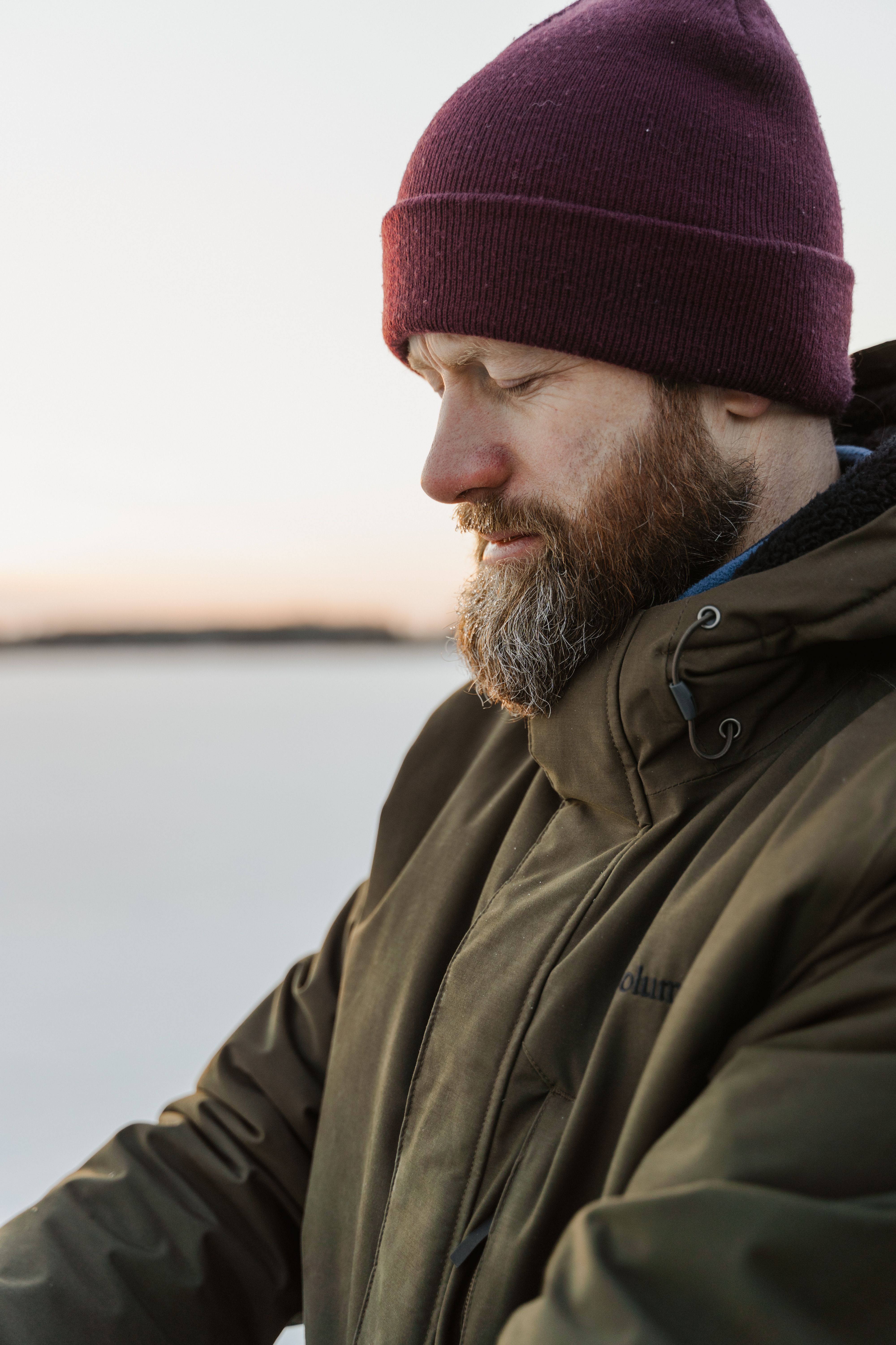 A thoughtful bearded man in a beanie and jacket outdoors during winter.