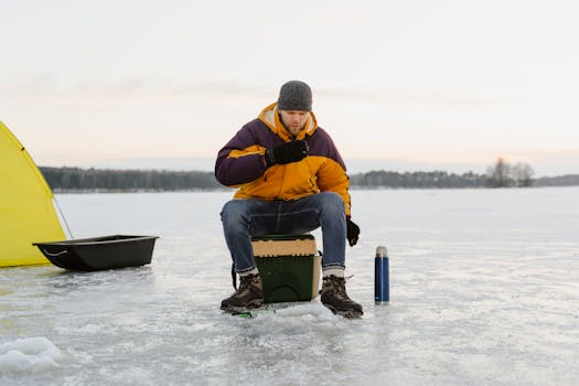 A man enjoys ice fishing on a frozen lake, surrounded by snow and winter scenery.