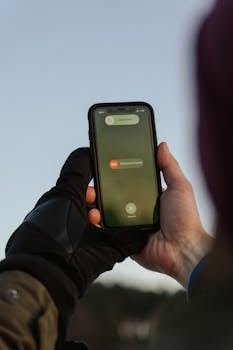 Person with gloves holding smartphone displaying emergency call option outdoors